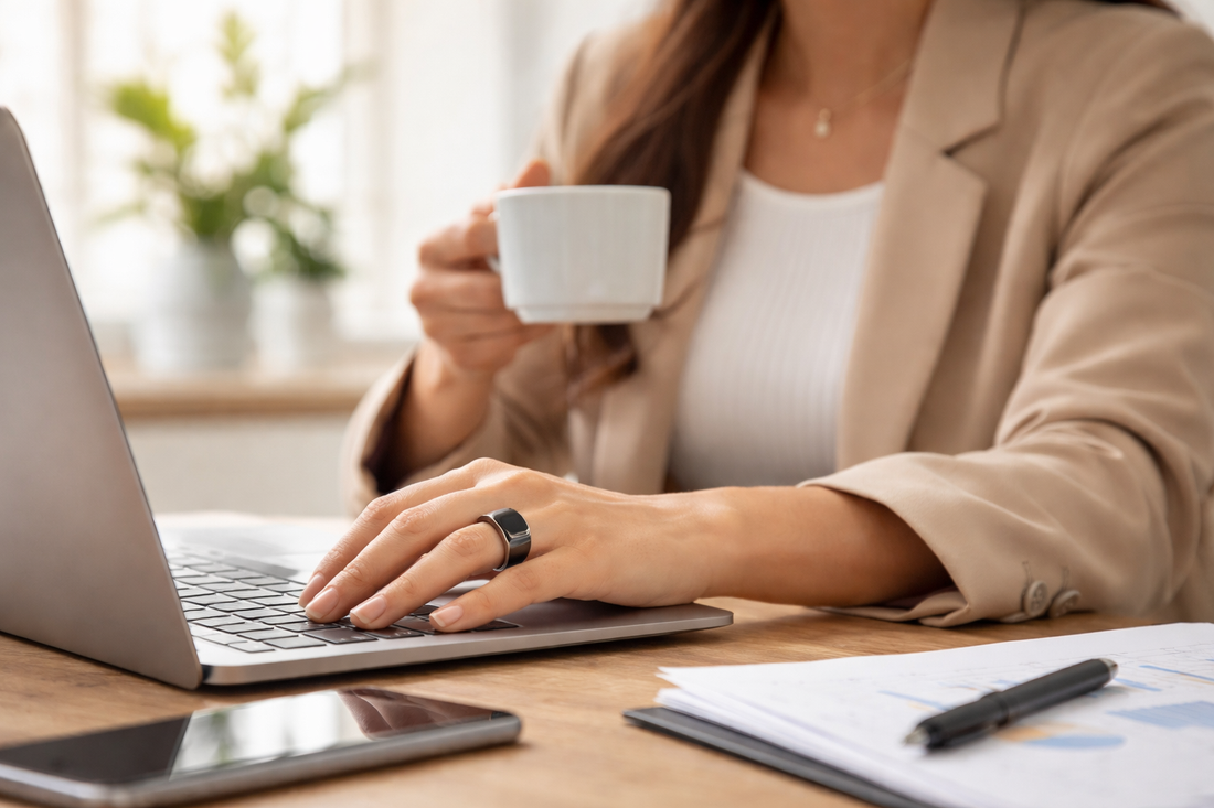 Person wearing a smart fitness ring while working on a laptop at a desk, showing discreet health tracking during everyday office work.