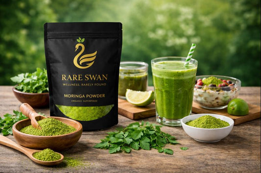 Rare Swan Moringa powder displayed with a green smoothie, fresh leaves, and prepared foods on a wooden table, showing how moringa powder can be used in daily diets.